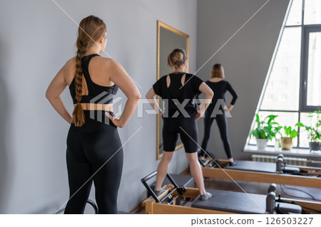 Young caucasian women exercising on pilates reformers in a bright studio. Their workout focuses on core strength and flexibility in a modern fitness environment. 126503227
