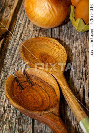 Rustic kitchen still life featuring wooden salad servers, a whole onion, and a carton of brown eggs, set against a weathered wooden surface. Rustic kitchen still life featuring wooden salad servers, a whole onion, and a carton of brown eggs, set against a weathered wooden surface. 126503318