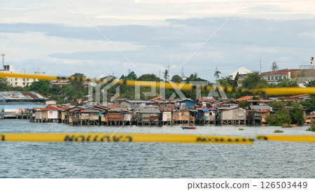 Slum area along the shore with yellow caution tape and greenery in foreground  126503449