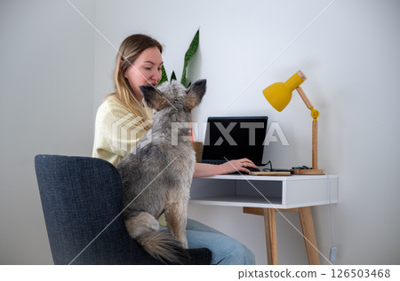 Women works from home with dog on lap at desk at home, concept of remote work and pet companionship 126503468
