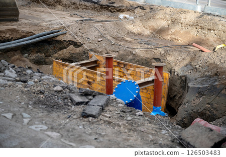 Underground pipeline construction site with trench shoring and blue valve exposed 126503483