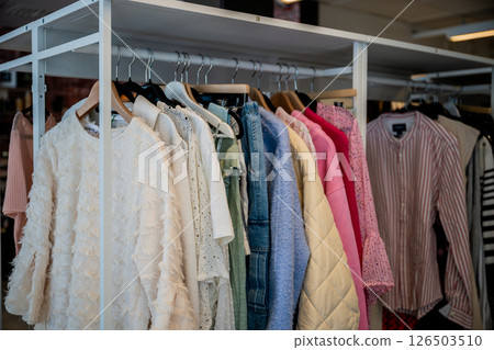 women's summer clothing in various colors and fabrics hanging on hangers in thrift shop. Second hand 126503510