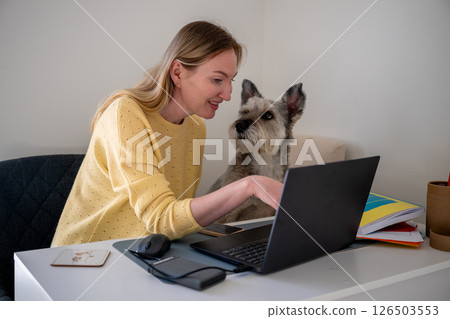 Woman working at a white desk in a home office while her dog sits on a nearby chair at cozy home Woman working at a white desk in a home office while her dog sits on a nearby chair at cozy home 126503553
