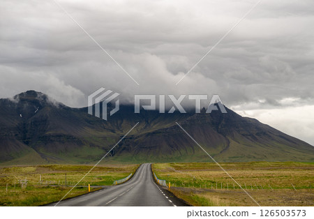 Empty road leading to misty mountain range under dramatic cloudy sky in Iceland 126503573