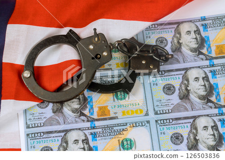 Handcuffs on US hundred dollar bills American flag serious mood evokes cautionary feelings about finance law. Handcuffs on US hundred dollar bills American flag serious mood evokes cautionary feelings about finance law. 126503836