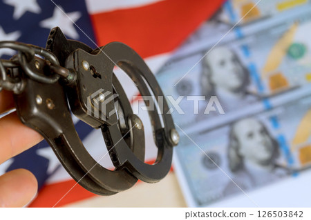 Handcuffs held firmly with counterfeit US money in background serious mood reflects caution apprehension 126503842
