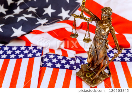 Statue of Justice stands solemnly indoors, holding scales sword with American flag drapes in background, evoking feelings patriotism justice. Statue of Justice stands solemnly indoors, holding scales sword with American flag drapes in background, evoking feelings patriotism justice. 126503845