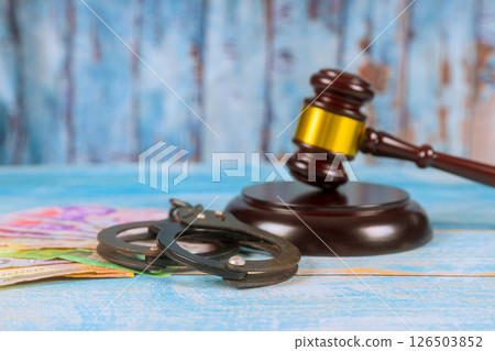 Gavel, handcuffs, money on wooden surface in courtroom serious mood reflects judicial themes legal consequences. 126503852