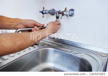 Man is replacing wall-mounted faucet spout using hands without tools while water traces remain near sink on metal countertop. 126503885