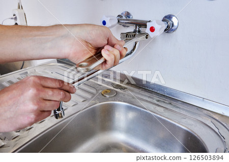 Using adjustable wrench plumber tightens mounting nut of spout on dual handle wall mounted faucet with hidden pipework inside wall. Using adjustable wrench plumber tightens mounting nut of spout on dual handle wall mounted faucet with hidden pipework inside wall. 126503894