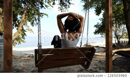 Happy woman ride on swing at tropical at sea beach. Carefree lady enjoying rest near ocean. Adult female having fun at sea shore on sunny day. Concept of summer vacation or holiday. Slow motion 126503960