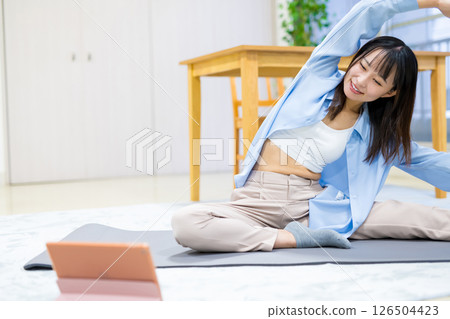 Young woman exercising at home while watching YouTube videos on tablet Yoga Stretching Diet Health 126504423