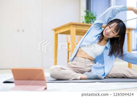 Young woman exercising at home while watching YouTube videos on tablet Yoga Stretching Diet Health 126504424