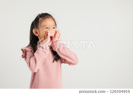 Asian happy portrait cute young kid girl standing hand on mouth talking news announcement studio shot isolated on white background, Thai kindergarten child announcement 126504959