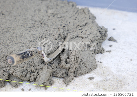 Close-up view of tiling tools: a trowel, pull tabs, and wedges lying on gray concrete, emphasizing the meticulous process of tile installation and leveling. 126505721
