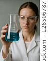 A female scientist in a lab studies a flask of bright blue liquid, conducting experiments 126506787