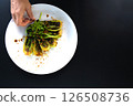 Hand adds finishing touches to a plate of bok choy with herbs in a stylish kitchen setting. 126508736