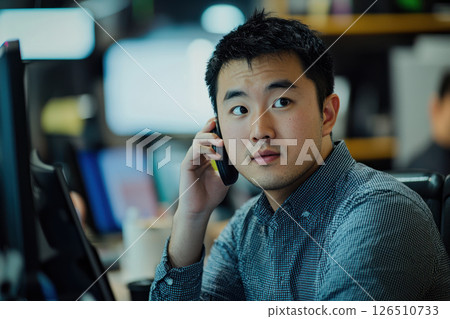 Young Asian professional on phone call in busy office environment, focused and engaged 126510733