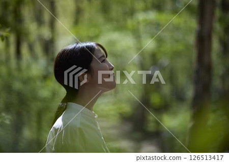 A woman's profile as she relaxes with her eyes closed in a lush green forest. A woman's profile as she relaxes with her eyes closed in a lush green forest. 126513417