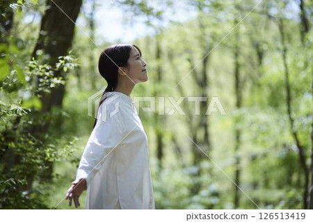 A woman takes a deep breath, bathed in sunlight filtering through the trees in a lush green forest. A woman takes a deep breath, bathed in sunlight filtering through the trees in a lush green forest. 126513419