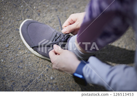 A woman tying her shoelaces before running in a lush green forest. A woman tying her shoelaces before running in a lush green forest. 126513453