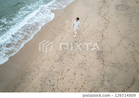 Aerial view of a man working remotely walking along the beach 126514809