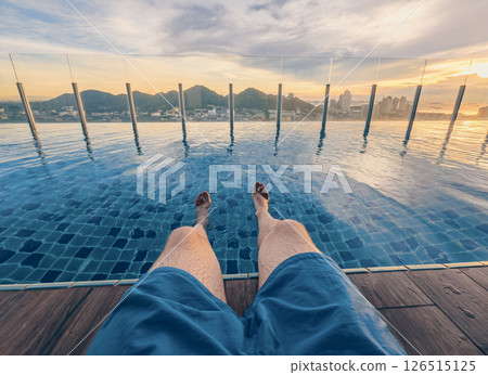 A person enjoys the tranquility of a pool during sunset. The horizon features mountains and a city skyline 126515125