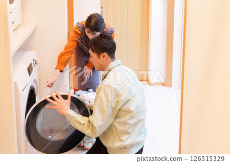 A customer having a professional repair his broken drum-type washing machine A customer having a professional repair his broken drum-type washing machine 126515329