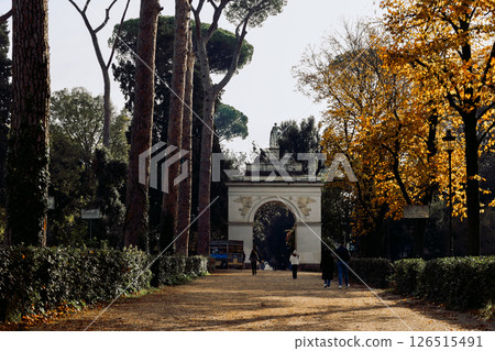 Serene scene of tranquil park surrounded by tall trees and prominent statue. Soft morning light filters through leaves, creating peaceful atmosphere. Villa Borghese gardens, Rome, Italy 126515491
