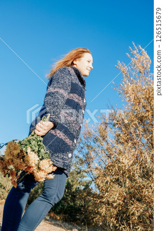Female portrait. Beautiful young girl with long dark hair walking with bouquet of flowers along beach on sunny autumn day. Vertical photo. High quality photo Female portrait. Beautiful young girl with long dark hair walking with bouquet of flowers along beach on sunny autumn day. Vertical photo. High quality photo 126515679