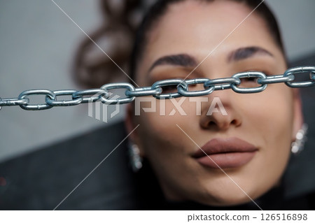 A striking close-up portrait of a fair-skinned woman with a chain partially obscuring her face, conveying a sense of constraint and mystery, with a minimalist aesthetic A striking close-up portrait of a fair-skinned woman with a chain partially obscuring her face, conveying a sense of constraint and mystery, with a minimalist aesthetic 126516898