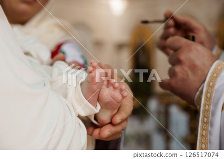 A tender moment during a baby's christening ceremony, where a priest anoints the infant's tiny foot with holy oil, symbolizing purification and acceptance into the faith A tender moment during a baby's christening ceremony, where a priest anoints the infant's tiny foot with holy oil, symbolizing purification and acceptance into the faith 126517074