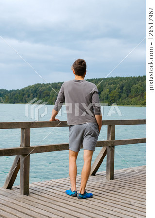 Young man standing near lake, view from back. Recreation in nature concept Young man standing near lake, view from back. Recreation in nature concept 126517962