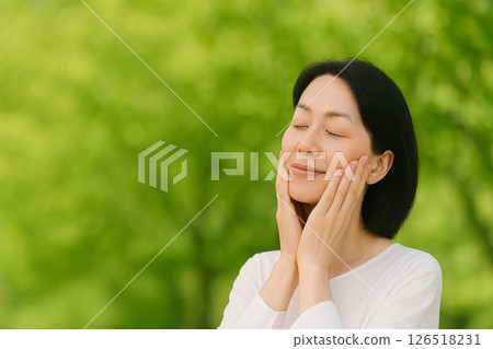A middle-aged woman feeling the moisture in her skin amidst fresh greenery 126518231