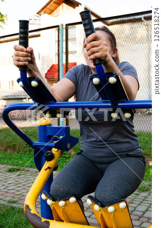 Woman exercising on outdoor fitness equipment. Strengthening arms and legs. 126518274