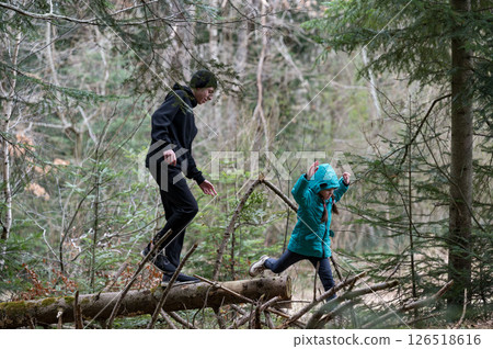 Exploring a tranquil forest with a child as they balance on fallen logs while enjoying the beauty of nature during a cloudy afternoon 126518616