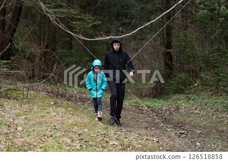 Two children explore a tranquil forest path on a chilly day, surrounded by lush greenery and fallen leaves, creating a moment of connection and adventure in nature Two children explore a tranquil forest path on a chilly day, surrounded by lush greenery and fallen leaves, creating a moment of connection and adventure in nature 126518858