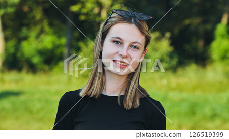 Smiling blonde teenage student in a black t shirt and sunglasses posing in a green park Smiling blonde teenage student in a black t shirt and sunglasses posing in a green park 126519399