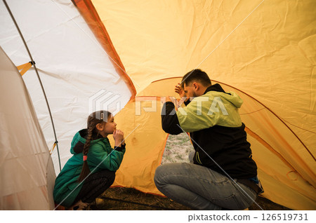 Father and daughter bond while setting up a vibrant tent during a weekend camping adventure in the serene wilderness as evening descends 126519731