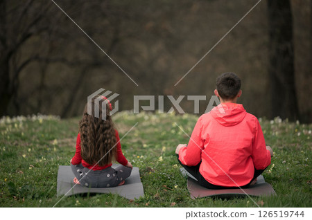 In serene moments of mindfulness, a girl and a boy practice meditation amidst lush greenery on a tranquil hillside during a peaceful afternoon In serene moments of mindfulness, a girl and a boy practice meditation amidst lush greenery on a tranquil hillside during a peaceful afternoon 126519744
