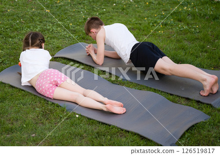 Kids doing plank exercises outdoors on yoga mats. Healthy lifestyle and fitness for children. 126519817