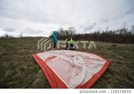 Setting up a cozy tent on a cloudy day in the countryside, creating memories and enjoying the great outdoors with a loved one Setting up a cozy tent on a cloudy day in the countryside, creating memories and enjoying the great outdoors with a loved one 126519839