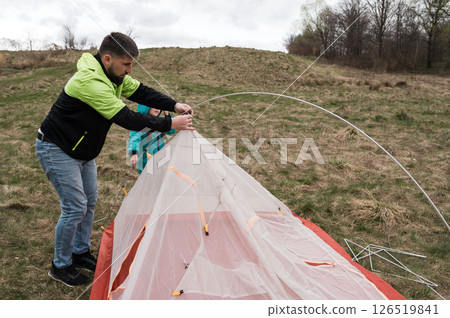 Setting up a cozy tent in the great outdoors on a cloudy day while enjoying the beauty of nature and the thrill of camping with friends Setting up a cozy tent in the great outdoors on a cloudy day while enjoying the beauty of nature and the thrill of camping with friends 126519841