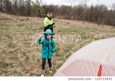 Setting up a cozy campsite on a cloudy day in early spring with a child learning the art of camping and bonding with nature in a lush green field 126519842