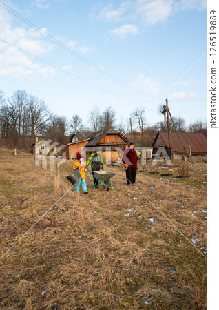 On a bright and sunny spring afternoon, a rural family can be seen collaborating diligently in the lush green fields adjacent to their charming countryside home 126519889