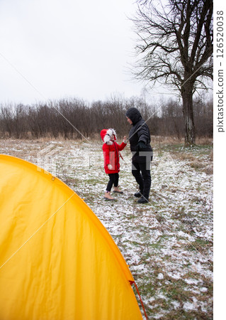 Winter adventure unfolds as a child in a red coat shares joy with a companion by a yellow tent in a snowy landscape, capturing a magical moment of togetherness Winter adventure unfolds as a child in a red coat shares joy with a companion by a yellow tent in a snowy landscape, capturing a magical moment of togetherness 126520038
