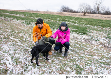 A couple delights in a beautiful winter day surrounded by nature, frolicking with their playful black dog in the snowy fields 126520142