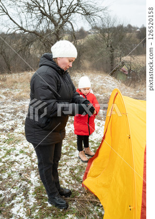 Mother and daughter set up a vibrant tent in the chilly countryside, showcasing teamwork and adventure in the great outdoors Mother and daughter set up a vibrant tent in the chilly countryside, showcasing teamwork and adventure in the great outdoors 126520158