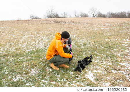 Joyful winter day with a dog and its owner in a snowy field enjoying playful moments outdoors in a rural setting surrounded by trees and grassland Joyful winter day with a dog and its owner in a snowy field enjoying playful moments outdoors in a rural setting surrounded by trees and grassland 126520385