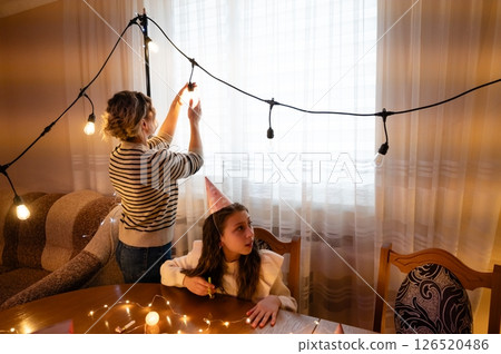 Preparing a cozy celebration with string lights and creativity in a warm living room during a festive evening Preparing a cozy celebration with string lights and creativity in a warm living room during a festive evening 126520486